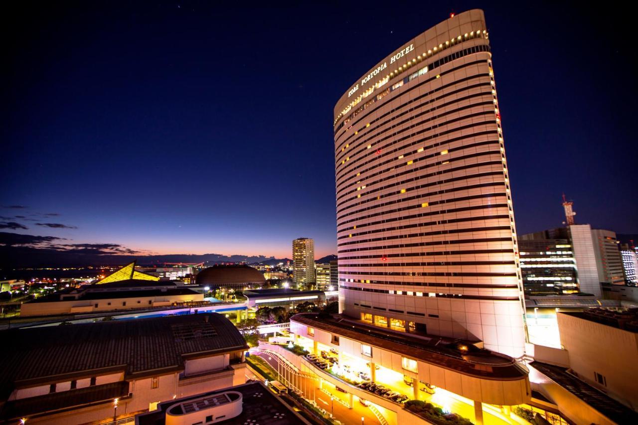 Kobe Portopia Hotel Exterior foto The photo shows a tall, modern hotel building illuminated at night. The hotel's facade features large windows and a sleek design, with lights illuminating its structure. In the foreground, there are some smaller buildings or structures, with a view o