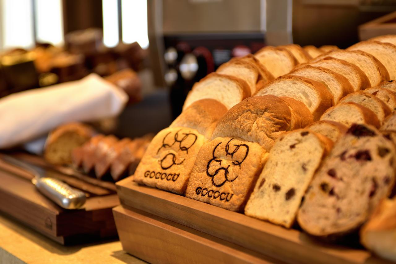 Kobe Portopia Hotel Exterior foto The image shows a display of various types of bread arranged neatly on a wooden serving tray. There are slices of bread, including some that appear to be toasted, and at least one slice features a decorative imprint with the word "GOOCCU." The backgr