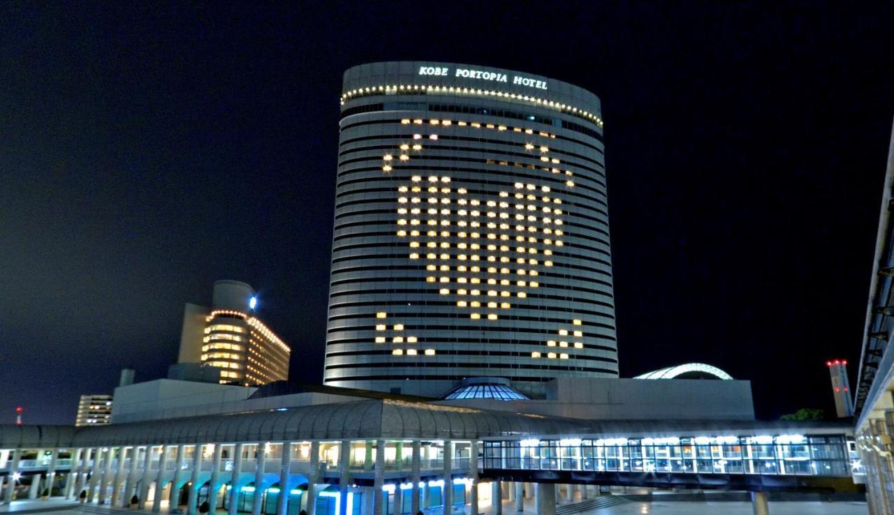 Kobe Portopia Hotel Exterior foto The photo shows a large hotel building at night, with illuminated windows forming a heart shape on its facade. The hotel is labeled as "Kobe Portopia Hotel." In the foreground, there is a structure that appears to be part of the hotel complex, along 